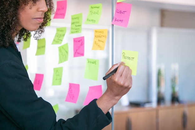 Cropped African American businesswoman writing on sticker with marker. Hand of office employer holding pen and making note