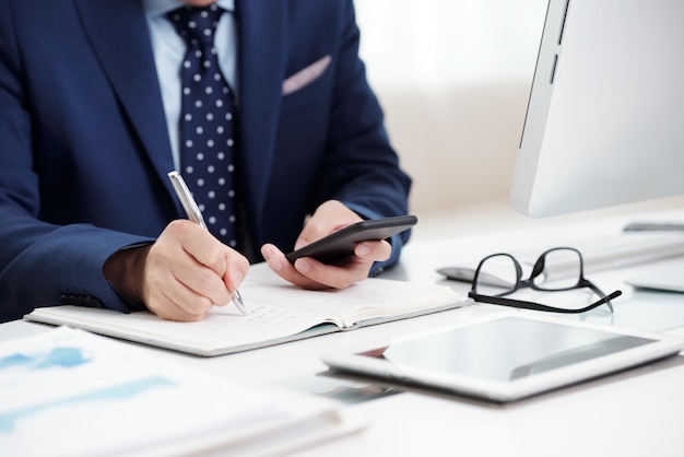 Free photo cropped business man making notes from his smartphone calendar to the organizer