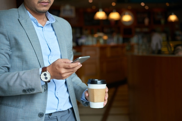 Cropped businessman checking phone mail holding takeaway coffee cup  in the morning