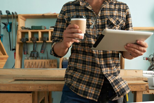 Foto gratuita carpentiere ritagliato con tavoletta digitale e caffè da asporto