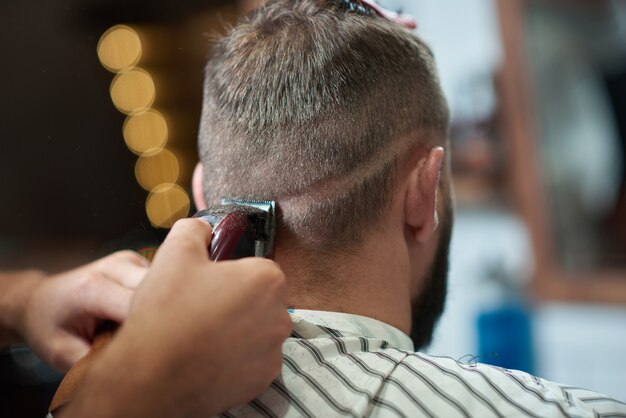 理髪店でプロの床屋が髪を整えている男性のクローズアップをトリミングしました。