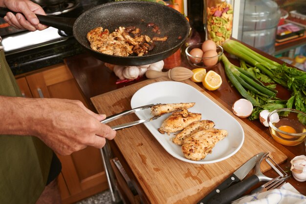 Cropped hands of anonymous cook transferring fried meat with tongs