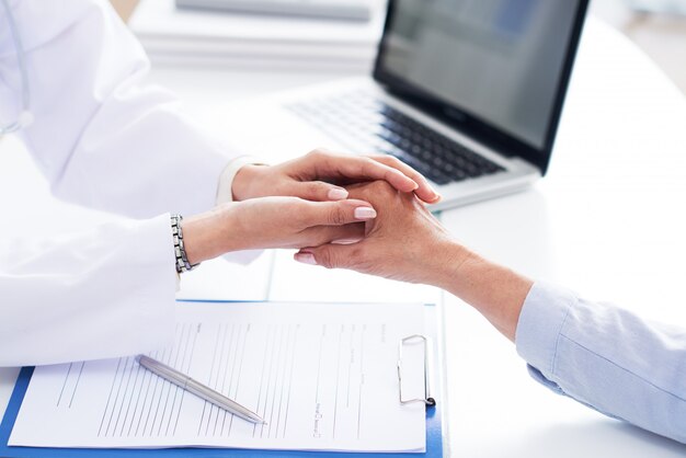 Cropped hands of doctor comforting unrecognizable patient 