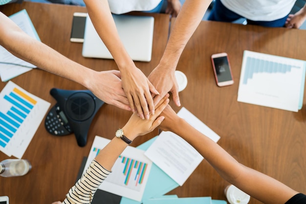 Обрезанное изображение коллег по бизнесу, складывающих руки над столом во время встречи в офисе