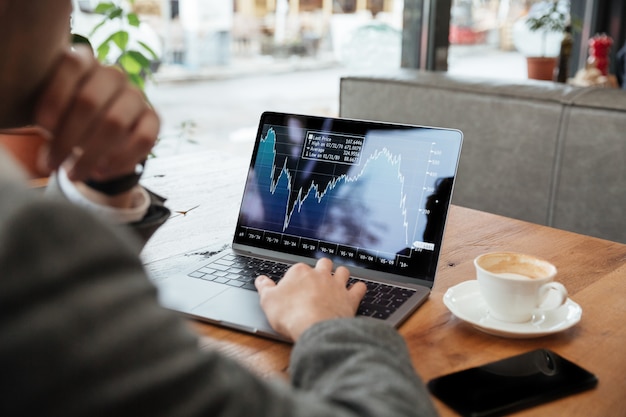 Cropped image of businessman sitting by the table in cafe and analyzing indicators