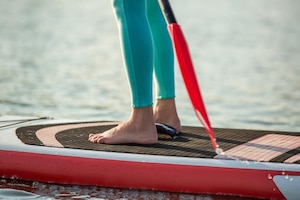 Cropped image of confident woman standing with a paddle on the surfboard, sup. sport. hobby. yoga.