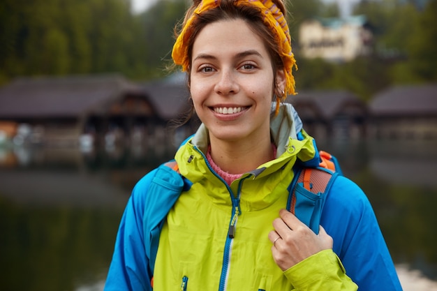 Free photo cropped image of delighted woman with toothy smile, wears casual jacket, carries rucksack