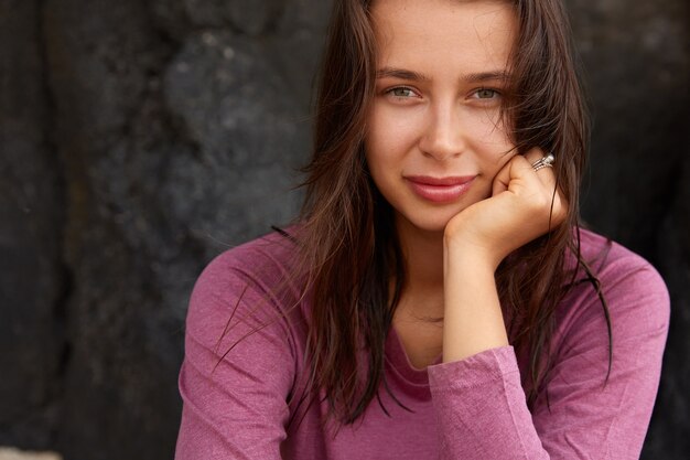 Cropped image of European woman holds chin, has dark hair and healthy skin