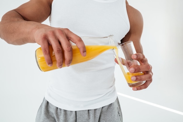 Cropped image of handsome young sportsman holding glass of juice.