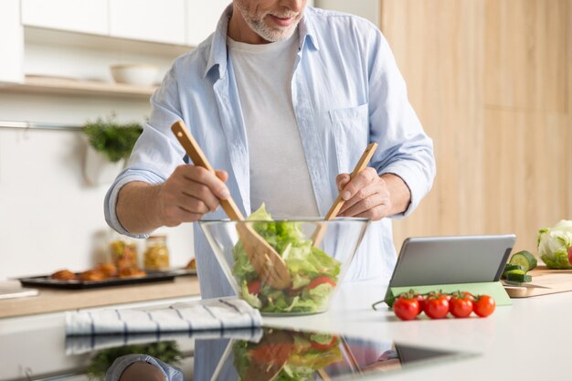 태블릿을 사용하여 샐러드를 요리하는 성숙한 남자의 자른 이미지