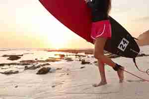 Бесплатное фото Обрезанное изображение спортивной женщины в шортах, которая выходит в океан с доской для серфинга на привязи