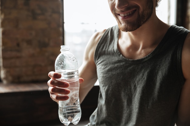 Foto gratuita immagine potata di una bottiglia di acqua sorridente della tenuta dell'uomo di forma fisica