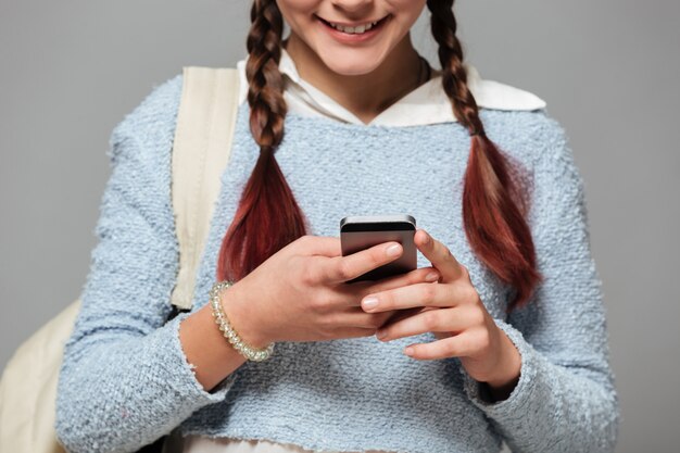 Обрезанное изображение улыбающейся школьницы с рюкзаком