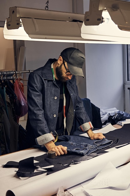 Cropped image of tailor makes measurements of jeans with a meter at sewing workshop.