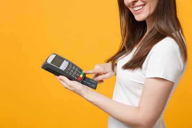 Cropped image of woman holding wireless modern bank payment terminal to process, acquire credit card payments isolated on yellow orange wall background. people lifestyle concept. mock up copy space.
