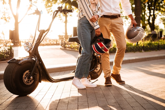 Cropped image of young african couple posing near the modern motorbike in park