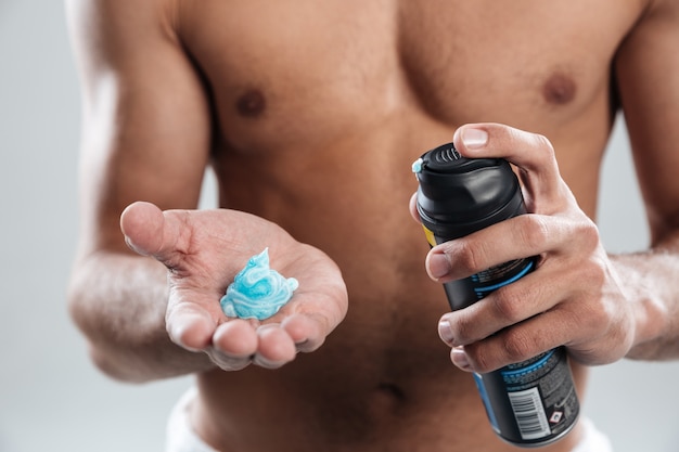 Cropped image of young man standing isolated holding shaving foam