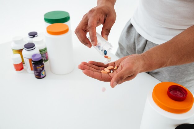 Cropped image of young sportsman holding vitamins and sport pills.