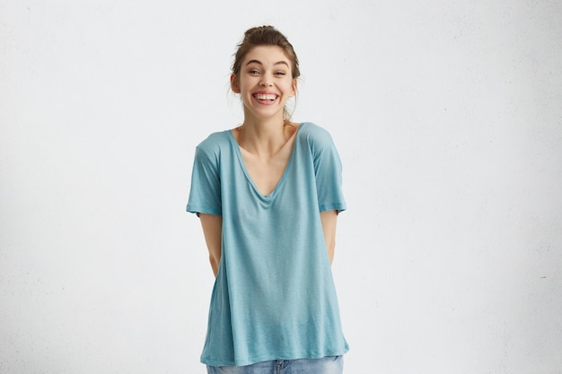 Free photo cropped isolated shot of charismatic and positive woman with easy cheerful smile holding hands behind her back, enjoying leisure time indoors