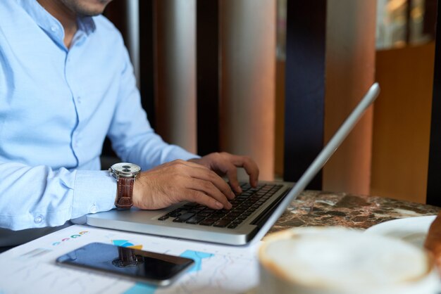 Cropped man busy typing on laptop keyboard having breakfast