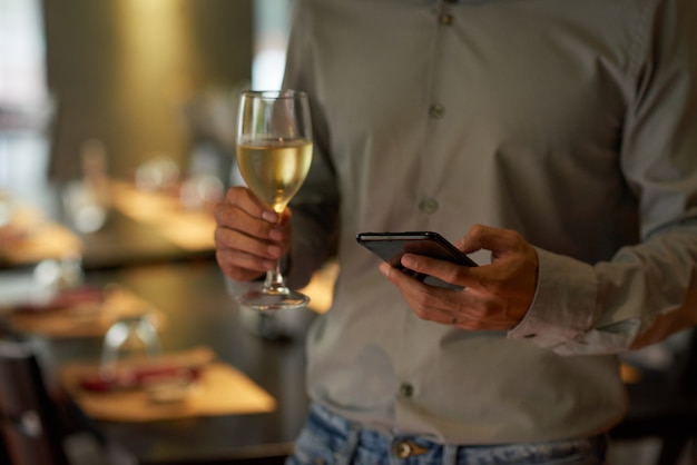 Cropped man checking phone holding champagne flute at a party