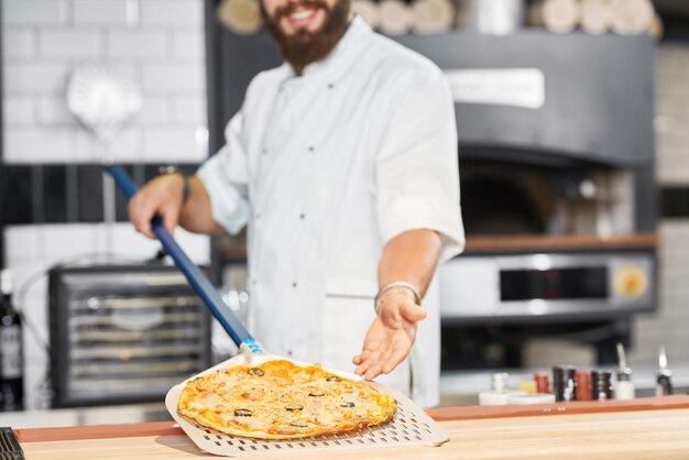 Cropped photo of baker holding fresh baked pizza laying on metallic shovel