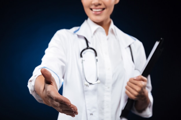 Подрезанное фото жизнерадостной медсестры держа доску сзажимом для бумаги и протягивает руку