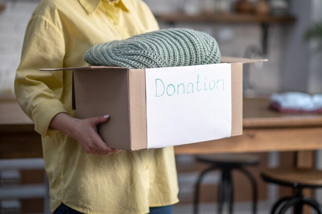 Обрезанное фото женщины-добровольца, держащей коробку с одеждой, подготовленной для пожертвований.