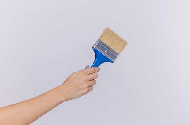 Cropped photo of hand of woman holding paint brush over isolated white wall