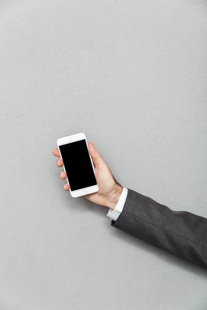 Cropped photo of male hand holding smartphone with blank screen isolated over gray, copy space