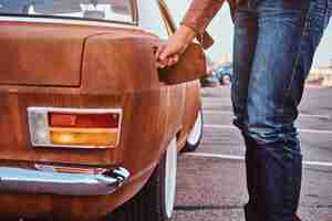 Free photo cropped photo of a male hand opens the gas cap of a tuned retro car for refueling.