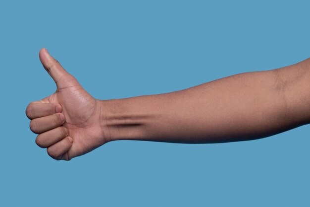 Cropped photo of a man holding the closed fist with the thumb extended upward on the blue background