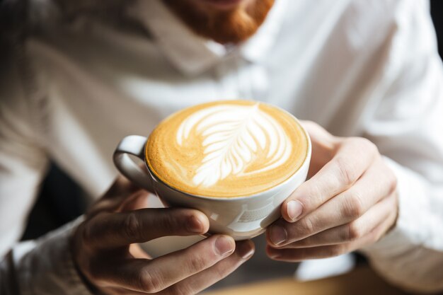 Cropped photo of man in white shirt holding hot coffee cup