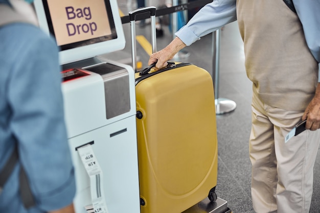Обрезанное фото двух пассажиров, распечатывающих багажную этикетку в киоске самообслуживания в аэропорту