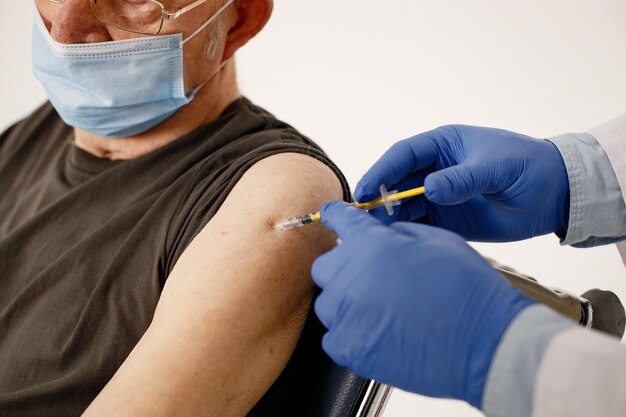 Cropped photo of old man's shoulder and doctor doing a vaccination
