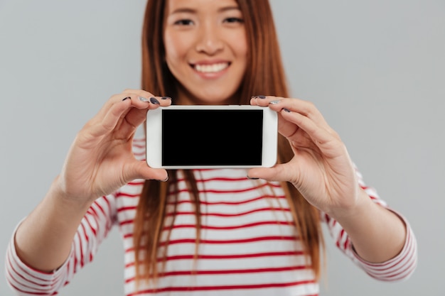 Cropped photo of smiling asian woman showing display of phone