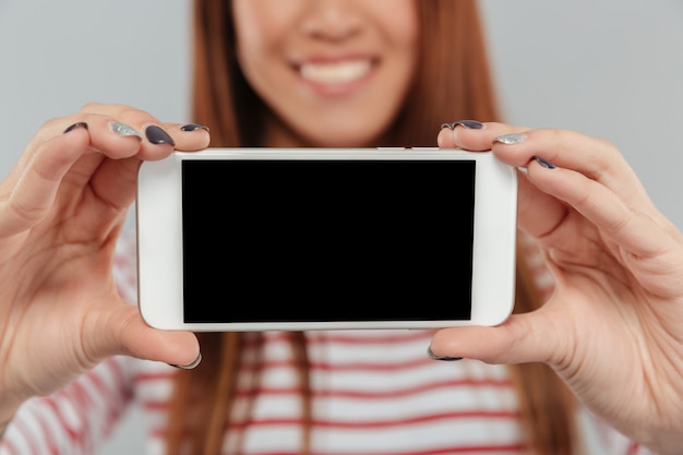 전화의 디스플레이를 보여주는 웃는 아시아 여자의 자른 사진