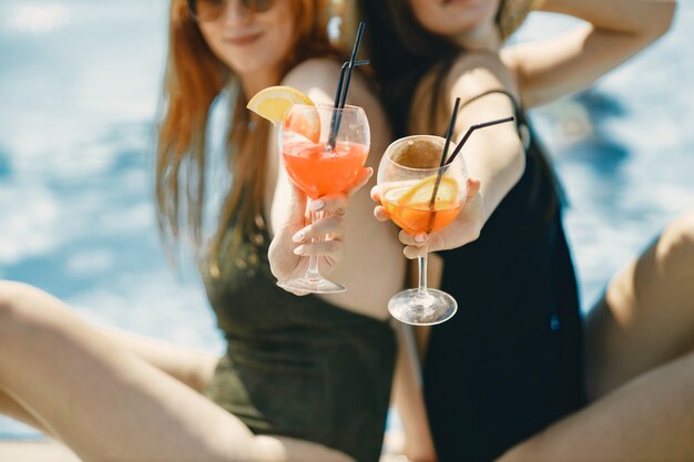 빨대와 함께 오렌지 음료와 함께 두 잔의 자른된 사진. 칵테일을 들고 수영복에 두 여자