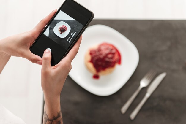 Cropped photo of woman make photo of pancakes by phone.