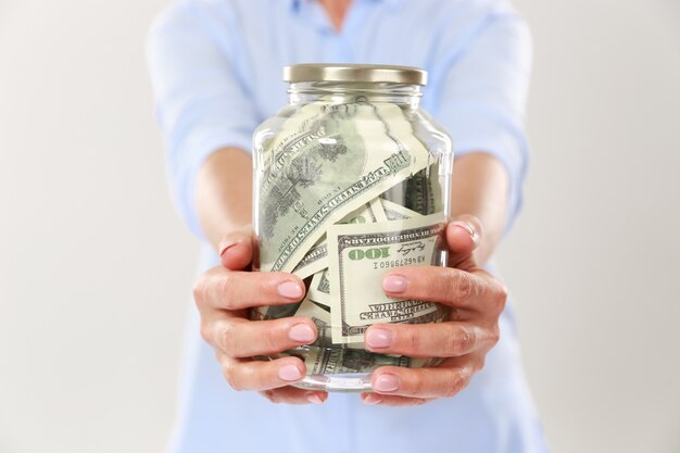 Cropped photo of womans hands holding glass jar with dollar bills