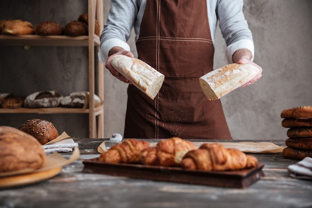 Cropped photo of young man baker holding bread.