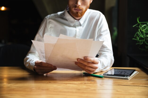 Подрезанное фото молодого readhead бородатого человека работая с бумагами