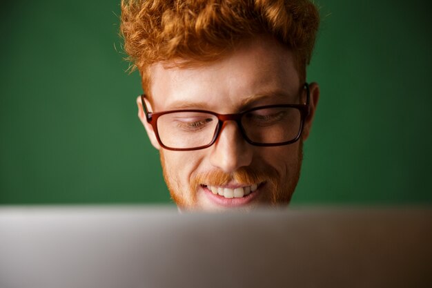 Cropped photo of young readhead man in glasses, working with laptop