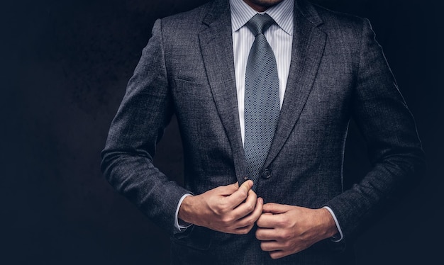 Cropped portrait of a successful businessman buttoning his elegant suit. Isolated on a dark background.