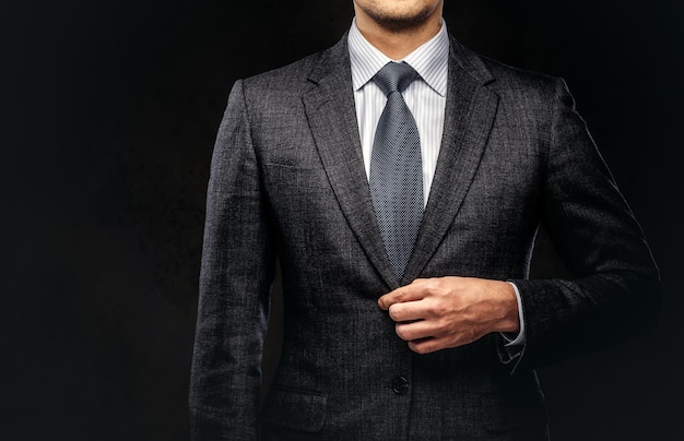 Cropped portrait of a successful businessman buttoning his elegant suit. Isolated on a dark background.