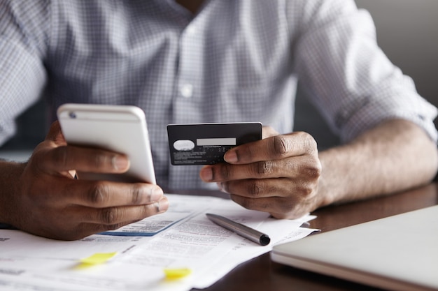 Cropped shot of African-American male paying bill at restaurant with online payment technology