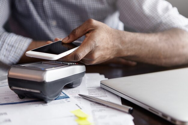 Cropped shot of African-American man paying bill at cafe, using NFC technology on mobile phone