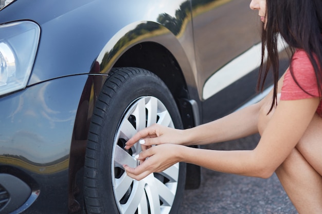 パンクした車のタイヤを変更しようとしているブルネットの女性ドライバーのショットをトリミング