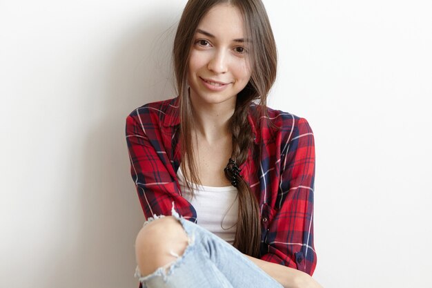 Обрезанный снимок милой кавказской девушки, смотрящей в камеру и застенчиво улыбаясь