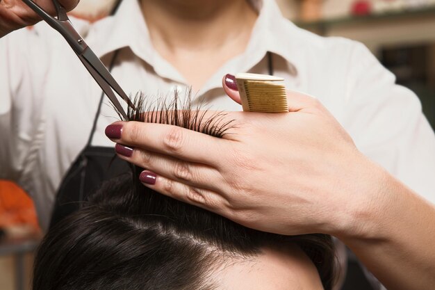 美容院でハサミで男の髪を切る女性美容師のトリミングショット。それらのスプリットエンドを取り除く。